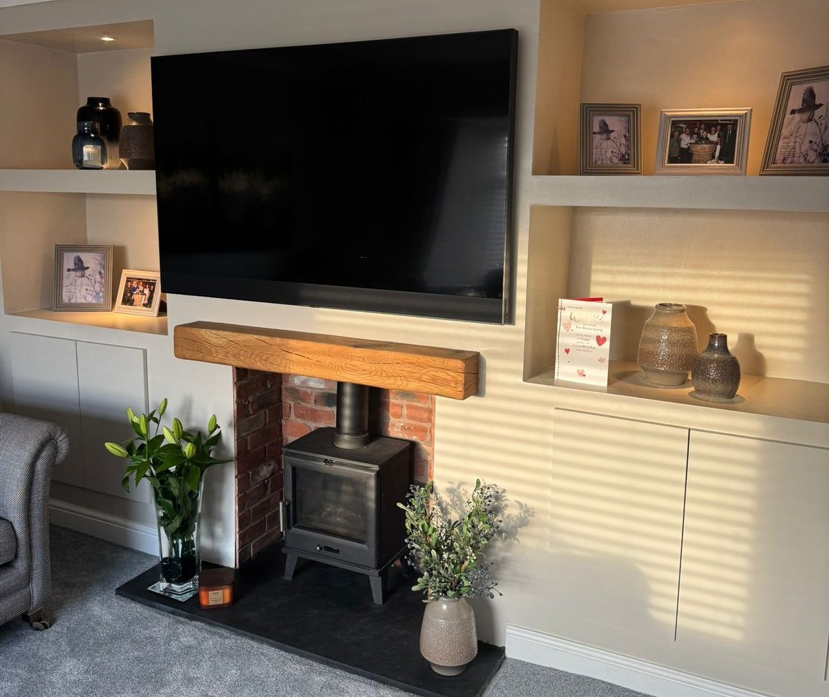 Fitted alcove joinery with lit display niches either side of a log burner by North West Media Walls